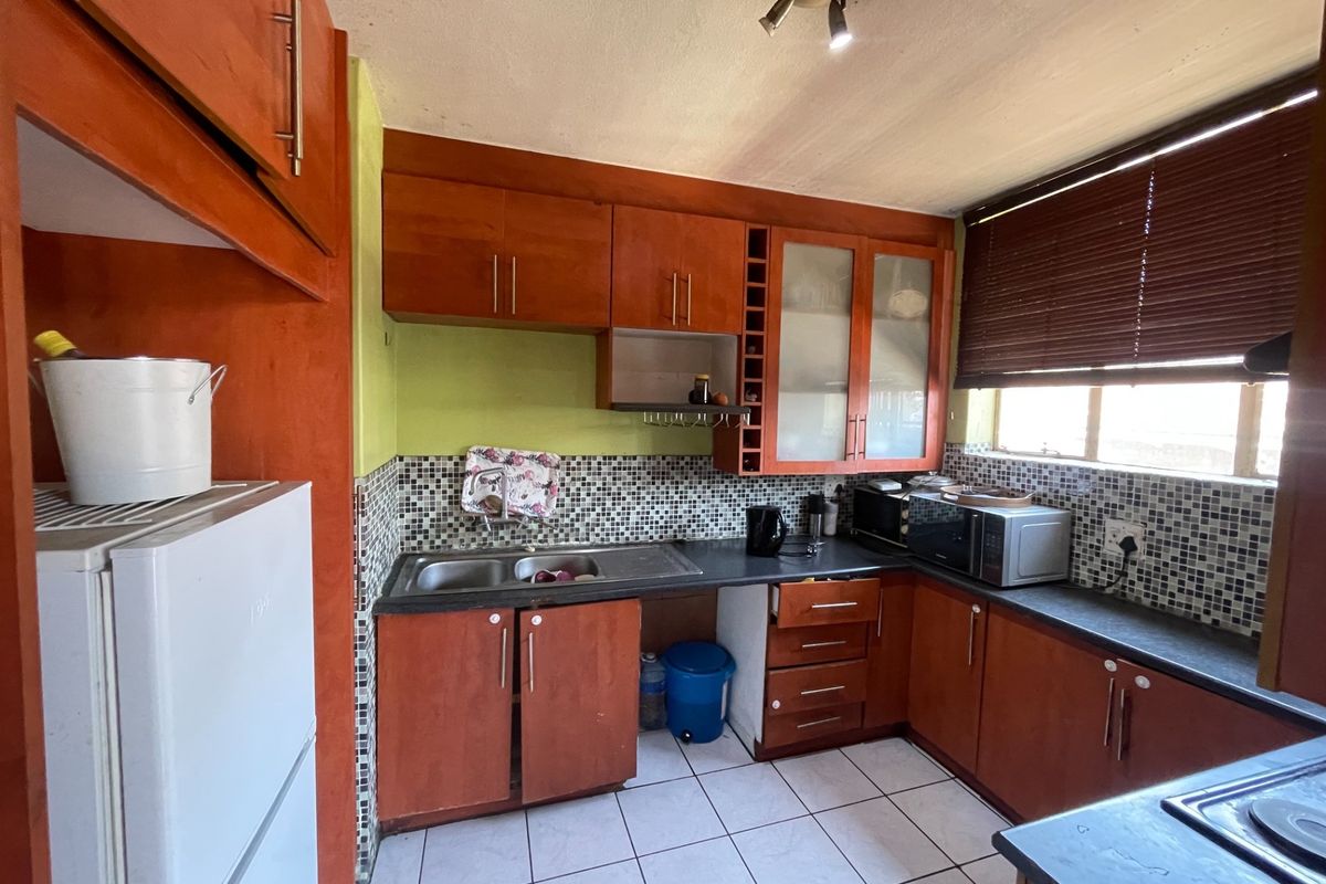A functional kitchen featuring wooden cabinetry, mosaic tile backsplash, double basin sink, and ceramic floor tiles, offering potential for modernization.