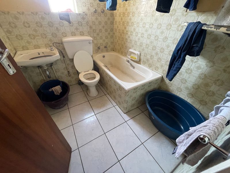 A dated bathroom featuring original ceramic wall tiles, a standard bathtub, pedestal basin, and toilet, requiring modernization and cosmetic updates.