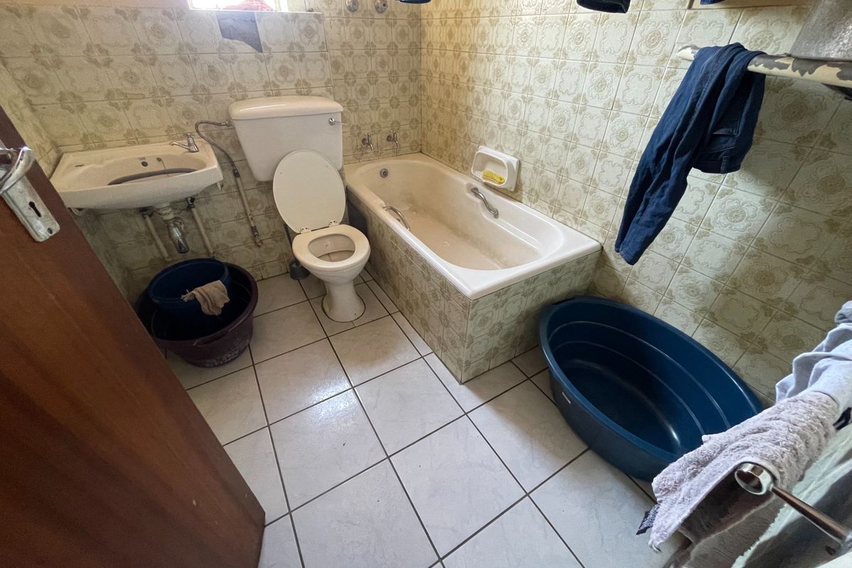 A dated bathroom featuring original ceramic wall tiles, a standard bathtub, pedestal basin, and toilet, requiring modernization and cosmetic updates.