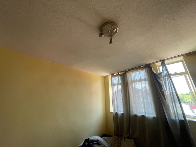 A simple bedroom space featuring a ceiling light fixture and a window, currently vacant and ready for renovation or restyling.
