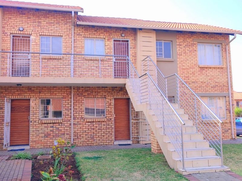 A well-maintained two-story apartment building featuring a face brick facade, external staircase with stainless steel balustrades, and a neat garden area.