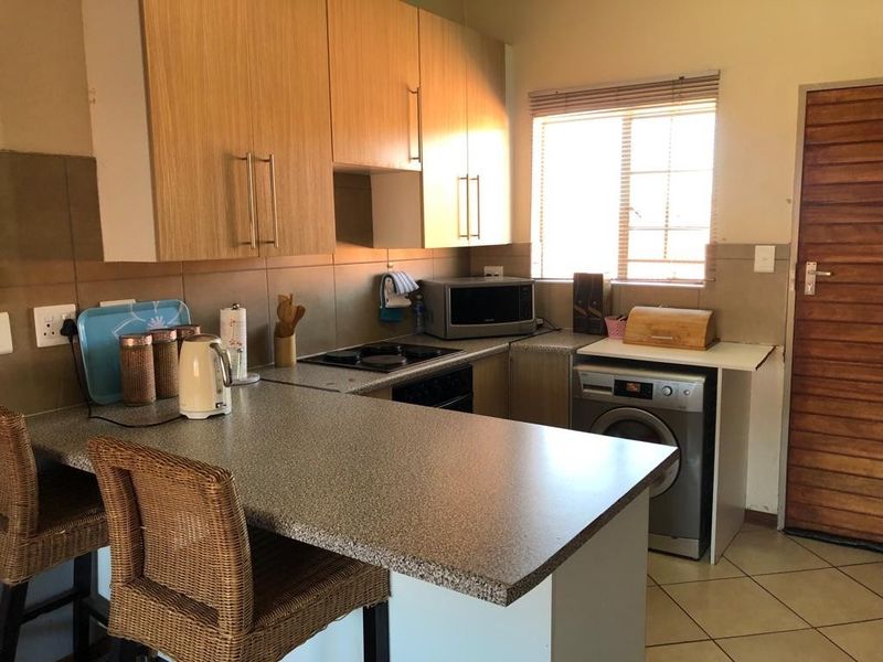 Functional kitchen featuring laminate cabinetry, stone-look countertops, built-in electric hob and oven, tiled backsplash, and ceramic floor tiles.