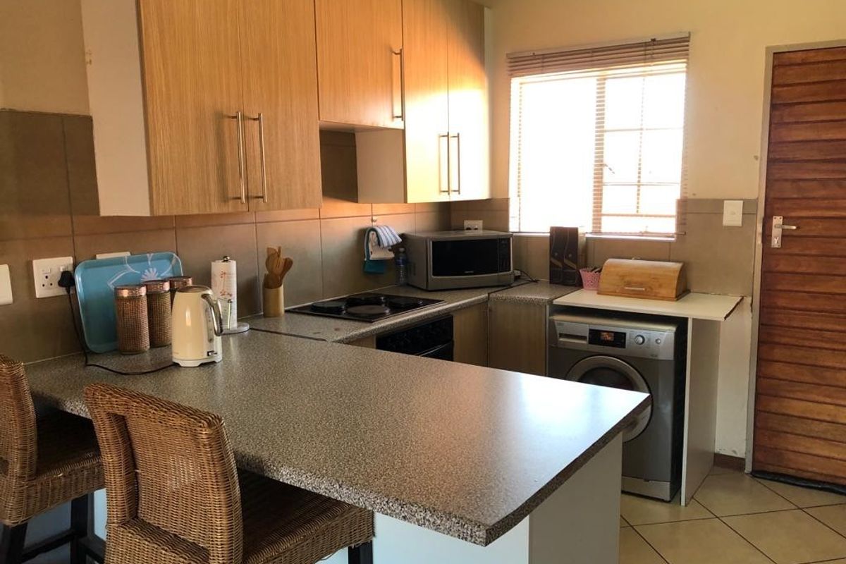 Functional kitchen featuring laminate cabinetry, stone-look countertops, built-in electric hob and oven, tiled backsplash, and ceramic floor tiles.