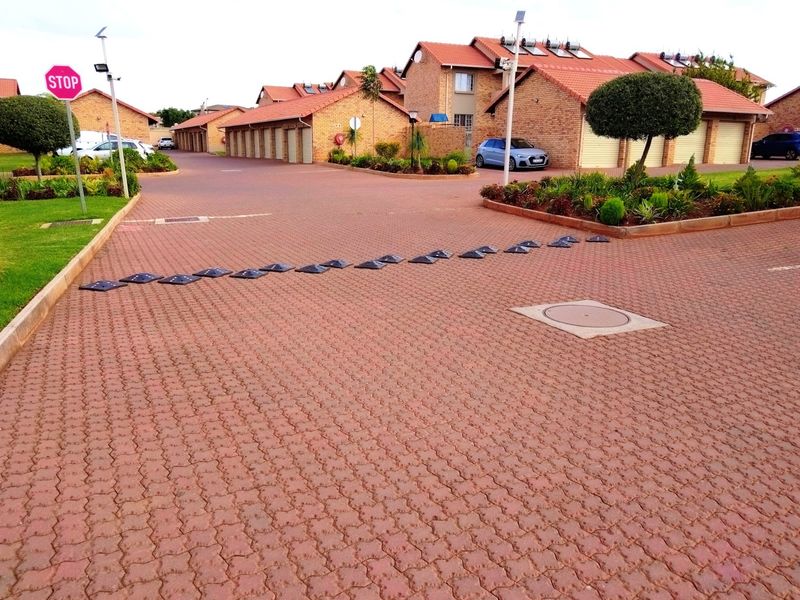 A well-maintained residential complex driveway featuring paved surfaces, speed bumps, and neat landscaping with brick-faced apartment units and garages in the background.