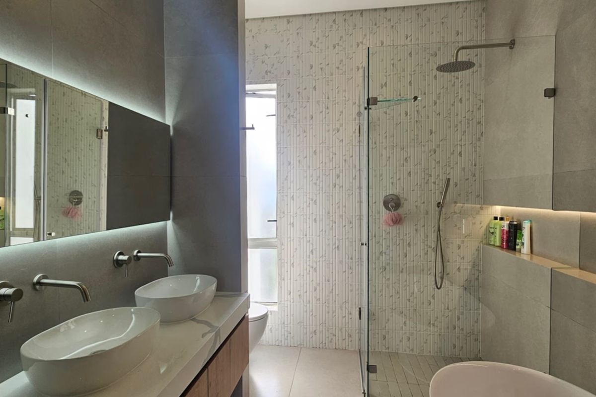 Modern bathroom featuring a double vanity with vessel sinks, wall-mounted faucets, backlit mirror, and a spacious walk-in shower with premium tiling.