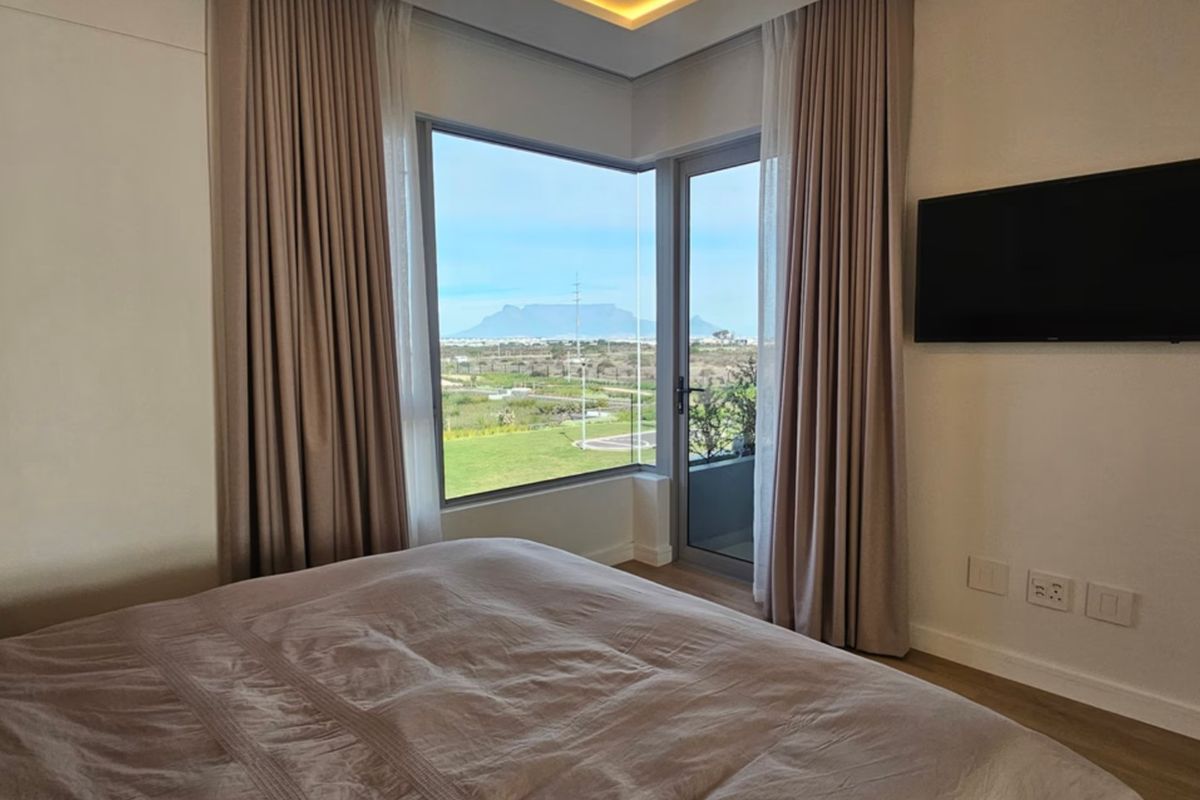 A modern bedroom featuring a corner window with scenic mountain views, recessed ceiling lighting, and direct access to an outdoor balcony.
