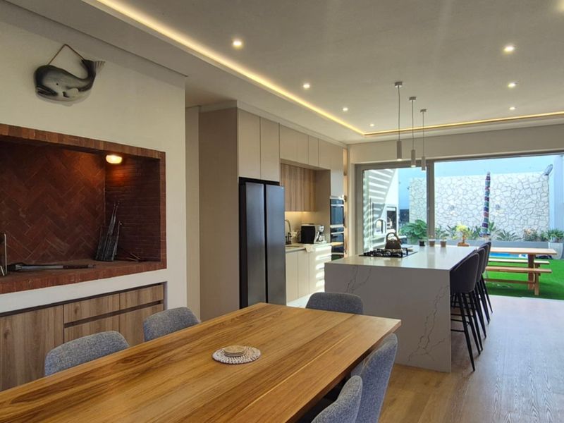 Modern open-plan living area featuring a sleek kitchen with stone island, built-in braai, and seamless flow to the outdoor patio and garden.