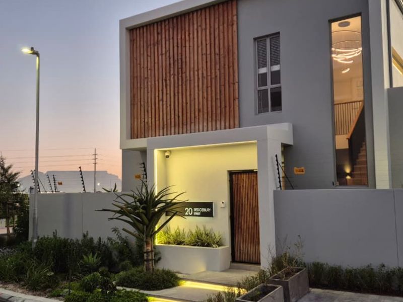 Modern two-story residential facade featuring timber cladding, clean architectural lines, integrated lighting, and secure boundary wall with electric fencing.