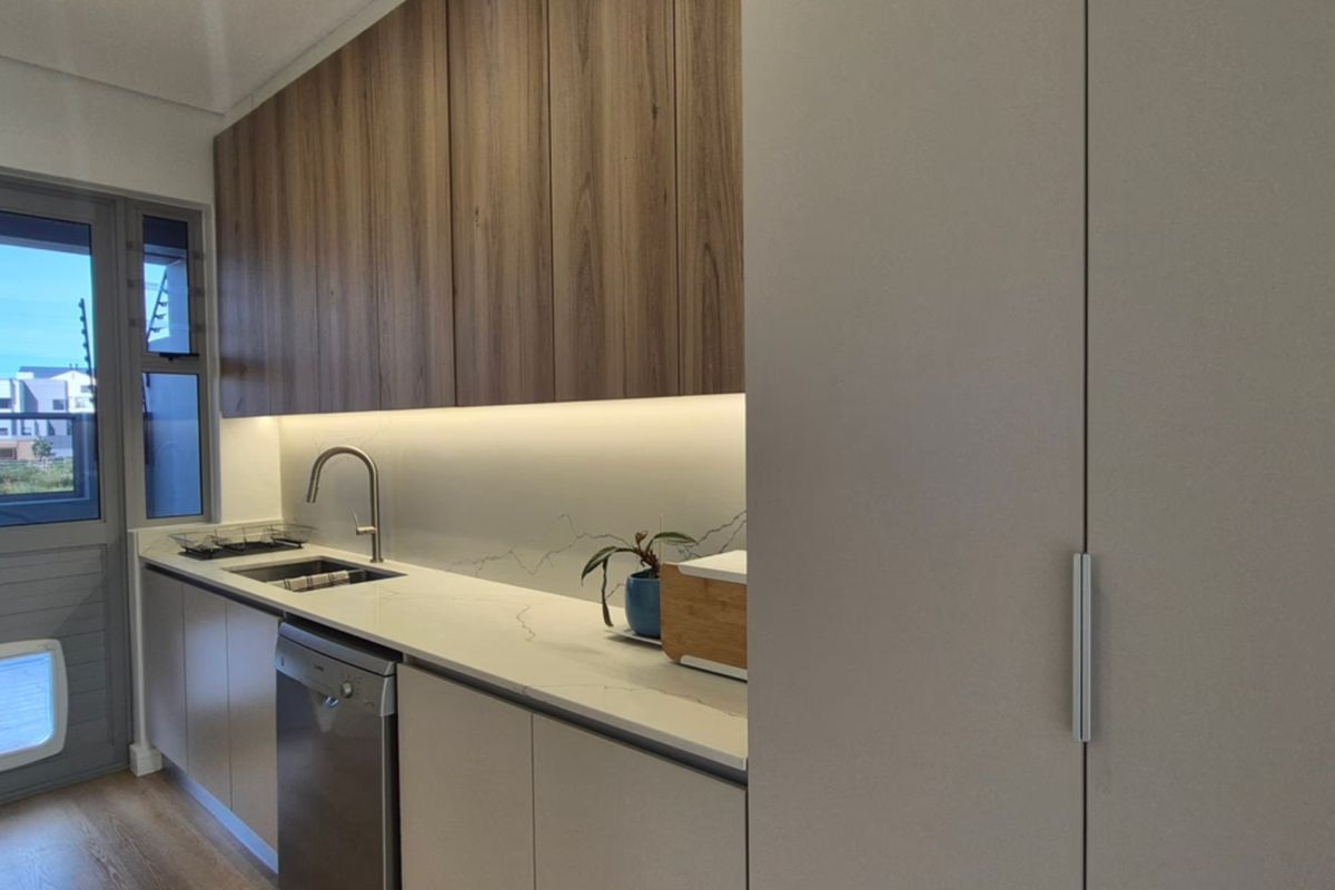 Modern kitchen featuring sleek wood-grain upper cabinetry, stone countertops, integrated dishwasher, and under-cabinet lighting, with direct access to the exterior.