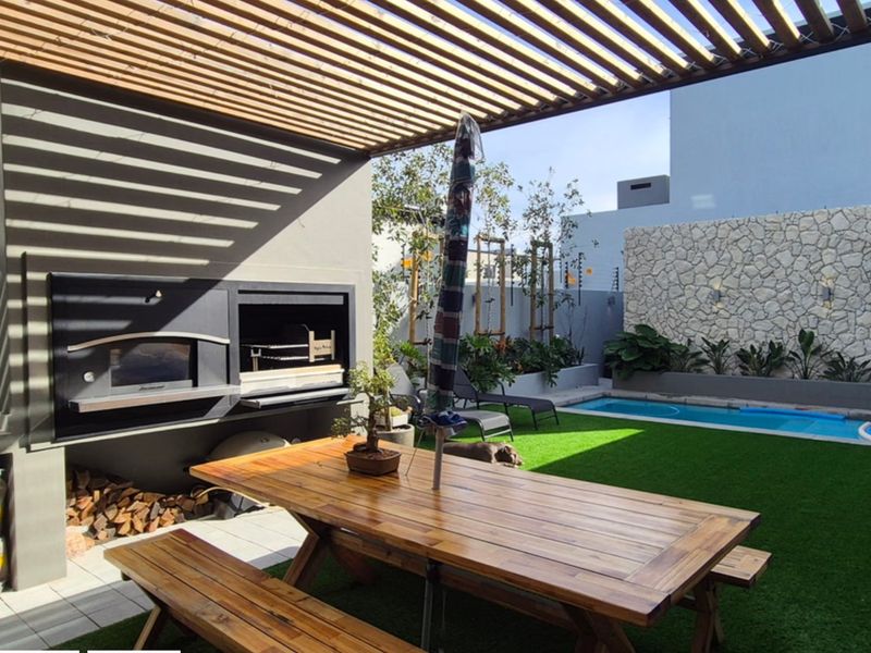 Outdoor entertainment area featuring a built-in braai, wooden pergola, swimming pool, and a decorative stone feature wall.