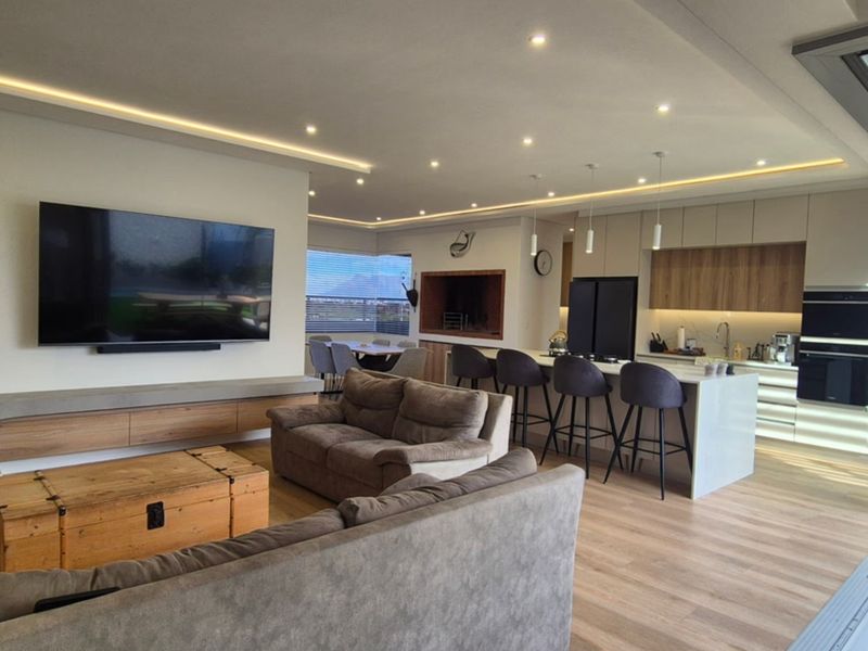 Modern open-plan living area featuring a sleek kitchen with island, built-in appliances, and seamless flow to an outdoor patio through large sliding glass doors.