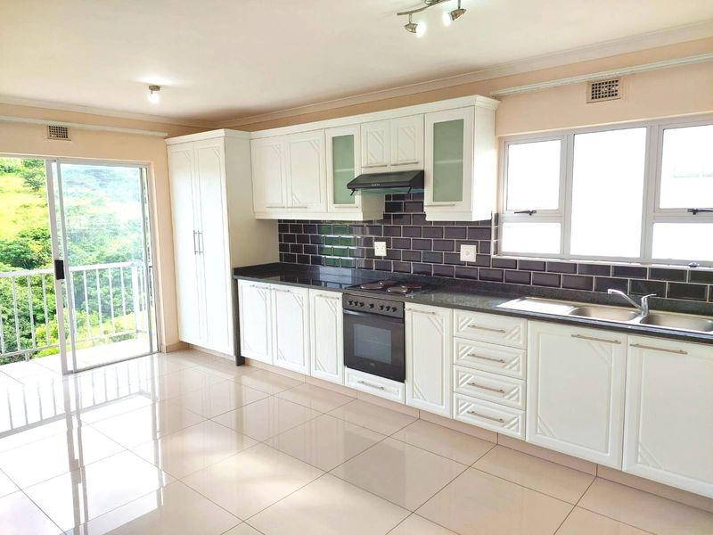 Modern kitchen featuring white cabinetry, dark granite countertops, subway tile backsplash, and integrated appliances, with direct access to a balcony.