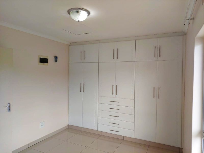 A clean, empty bedroom featuring extensive white built-in cupboards with integrated drawers and neutral tiled flooring.