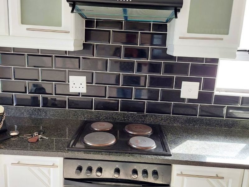 A well-maintained kitchen featuring white cabinetry, dark granite countertops, and a stylish black subway tile backsplash with a built-in electric stove and extractor fan.