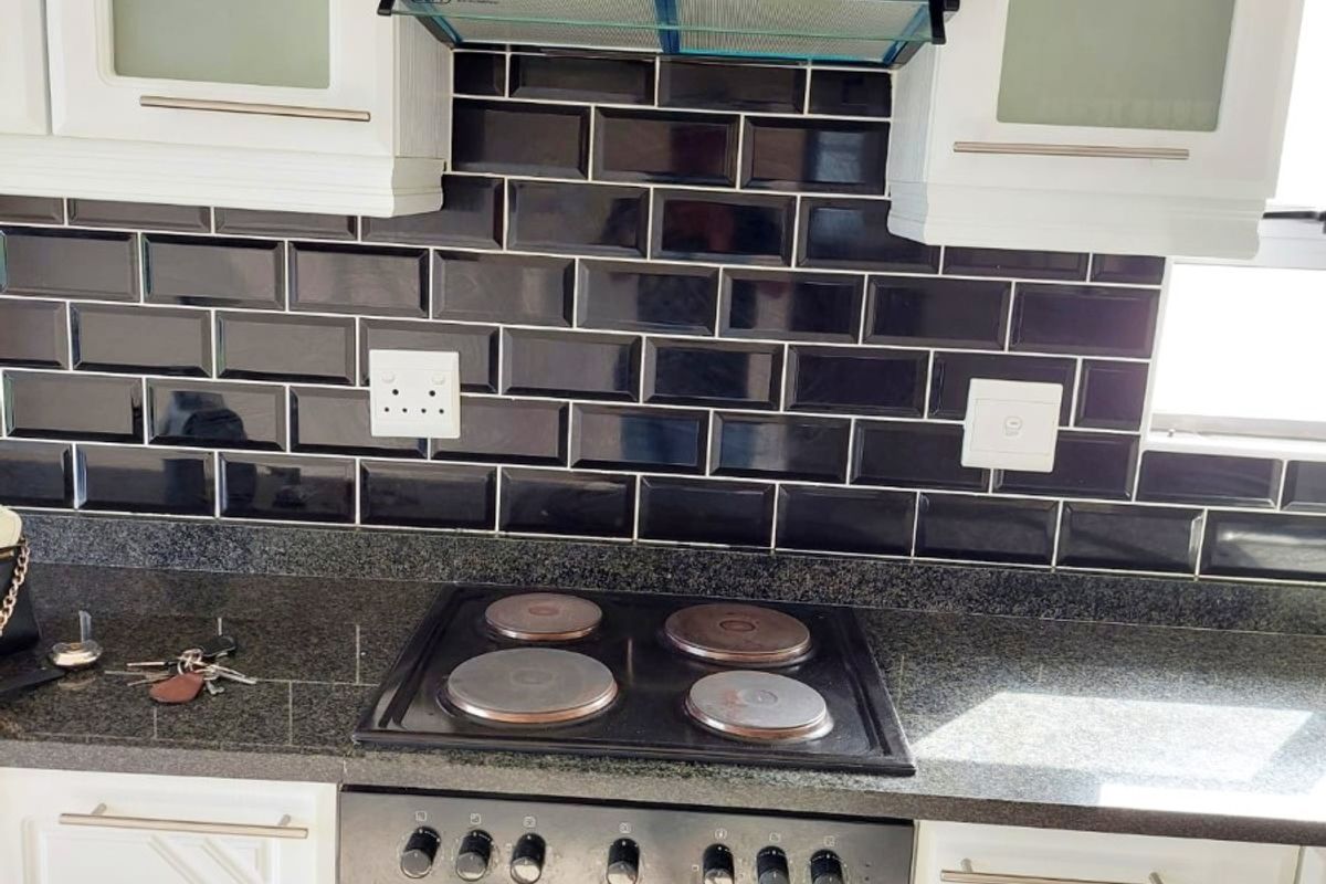 A well-maintained kitchen featuring white cabinetry, dark granite countertops, and a stylish black subway tile backsplash with a built-in electric stove and extractor fan.