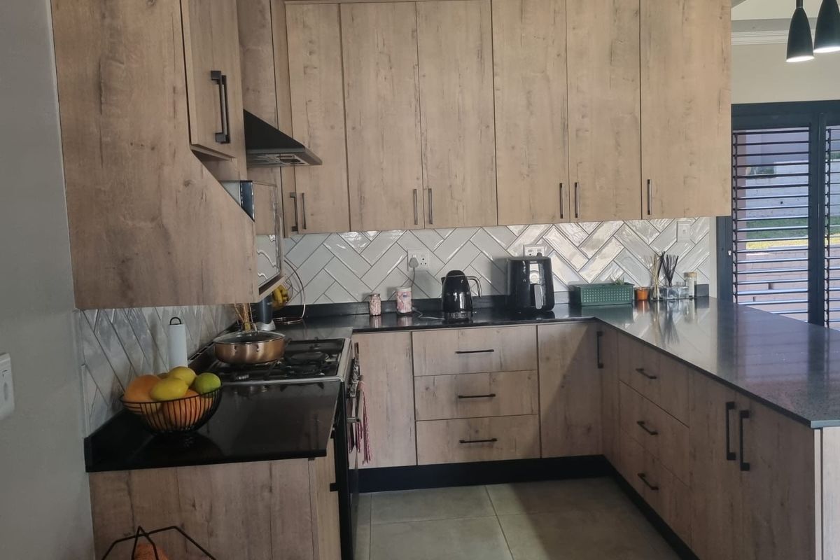 Modern kitchen featuring wood-look cabinetry, black granite countertops, and a stylish herringbone tile backsplash with integrated gas hob and oven.