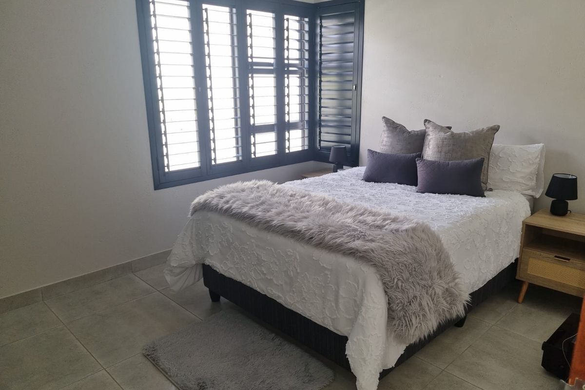 A well-maintained bedroom featuring neutral tiled flooring and dark louvered window shutters, providing a clean and functional living space.