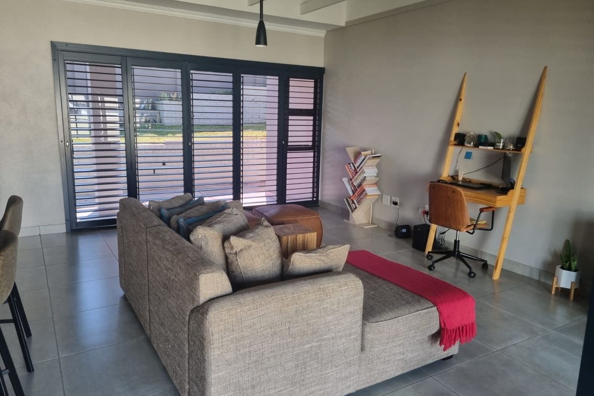Spacious living area featuring large aluminium stacker doors that provide seamless access to the outdoors, complemented by modern tiled flooring and exposed beam ceilings.