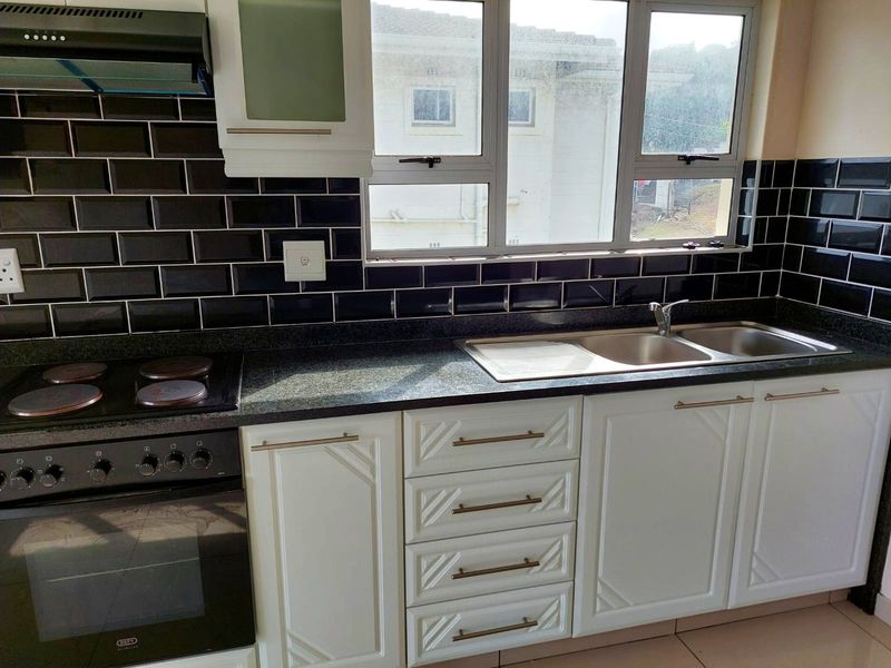 A well-maintained kitchen featuring white cabinetry, granite countertops, a black subway tile backsplash, and integrated stainless steel appliances.