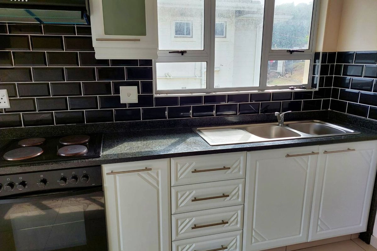 A well-maintained kitchen featuring white cabinetry, granite countertops, a black subway tile backsplash, and integrated stainless steel appliances.