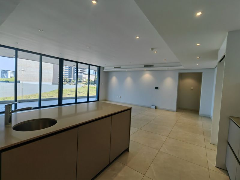 Spacious open-plan living area featuring a modern kitchen island, large format floor tiles, and floor-to-ceiling glass doors leading to an outdoor space.