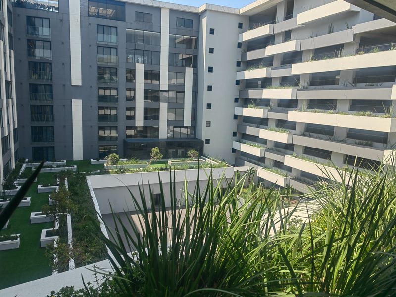 A view of the modern apartment complex courtyard featuring landscaped gardens, tiered balconies with glass balustrades, and contemporary architectural design.