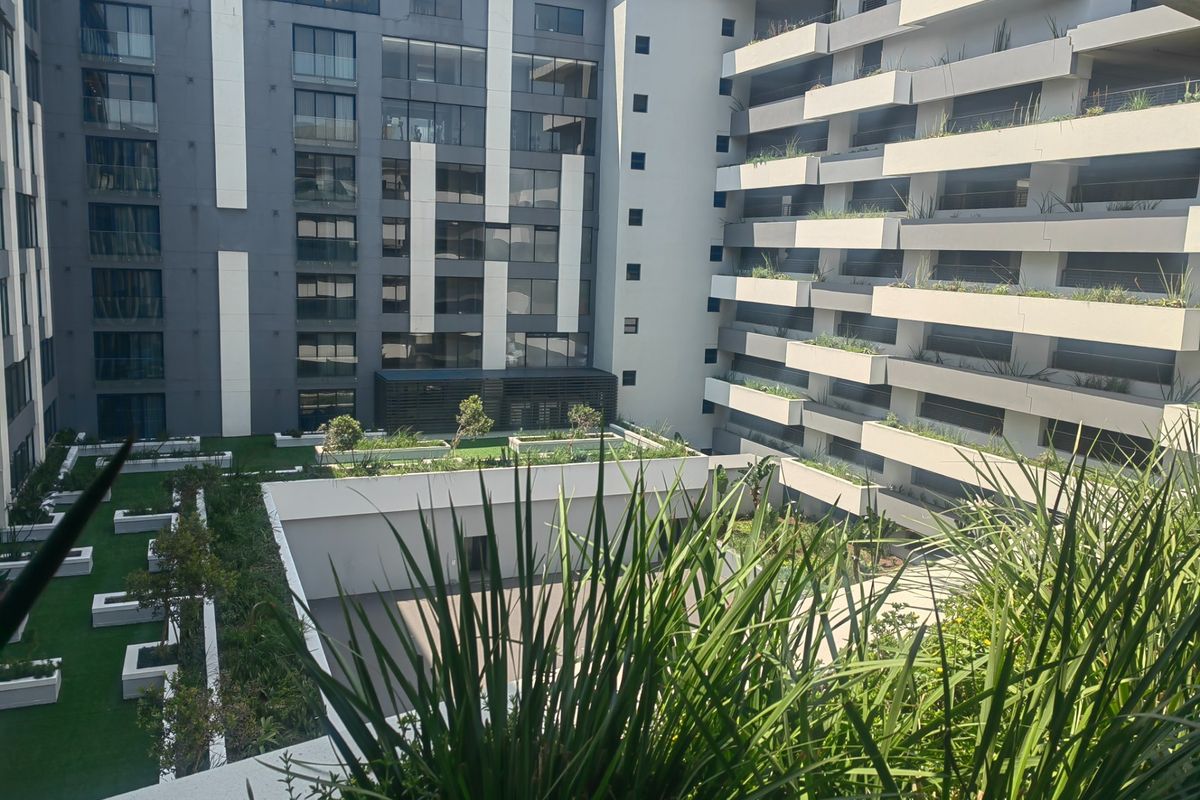 A view of the modern apartment complex courtyard featuring landscaped gardens, tiered balconies with glass balustrades, and contemporary architectural design.