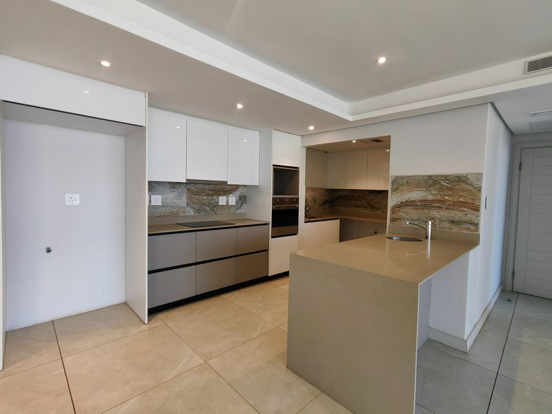 Modern kitchen featuring sleek cabinetry, stone countertops, integrated oven and hob, and a functional island with an undermount sink.