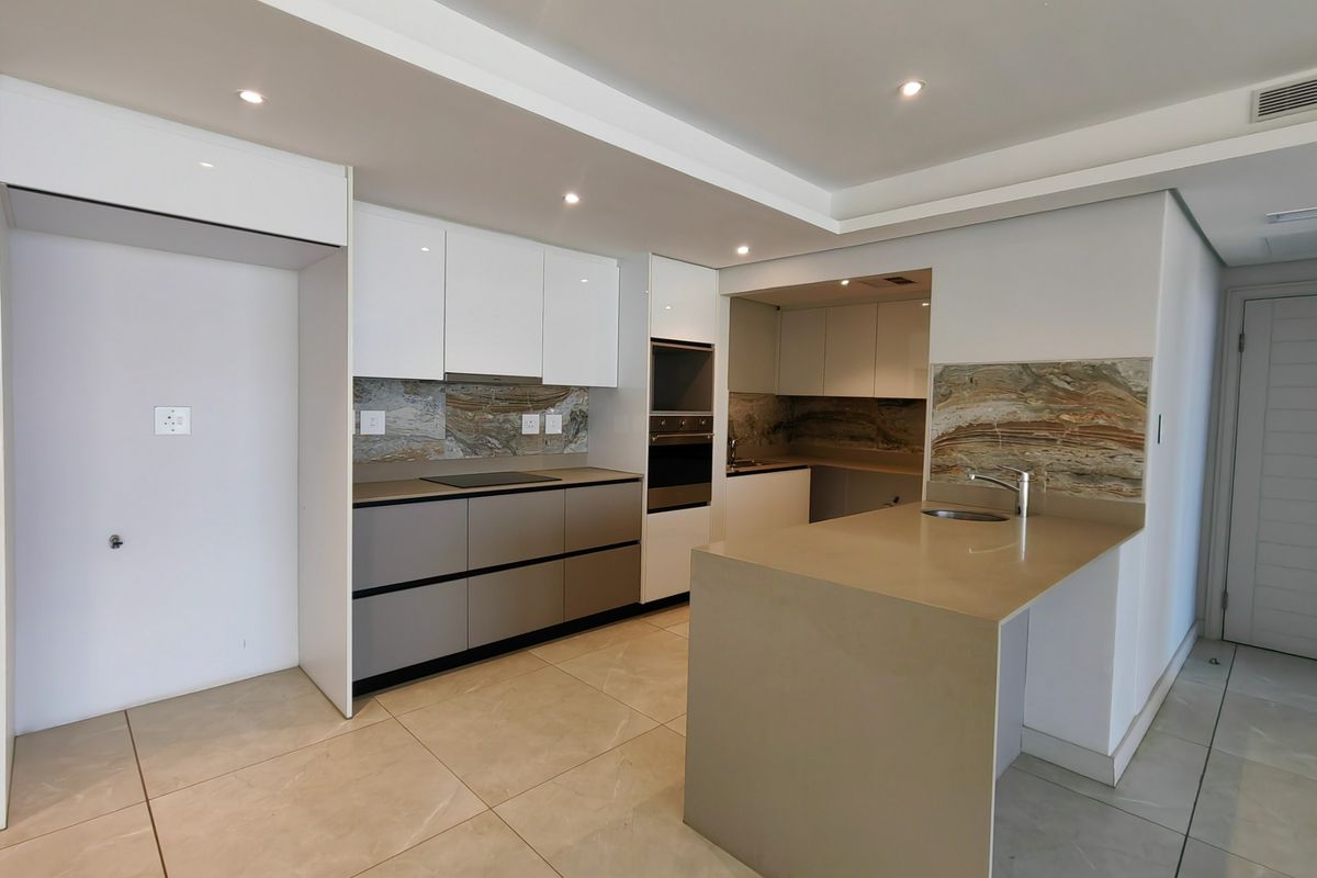 Modern kitchen featuring sleek cabinetry, stone countertops, integrated oven and hob, and a functional island with an undermount sink.