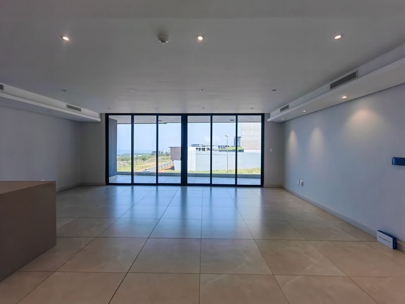 Spacious open-plan living area featuring large format floor tiles, recessed lighting, ducted air conditioning, and expansive sliding glass doors leading to an outdoor view.