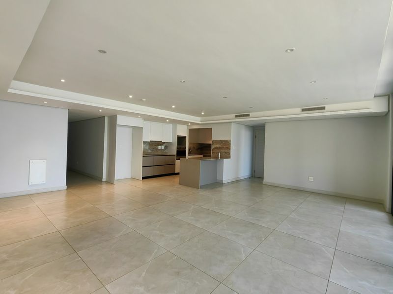 Spacious open-plan living area featuring large format floor tiles, recessed lighting, and a modern kitchen with built-in cabinetry and a central island.