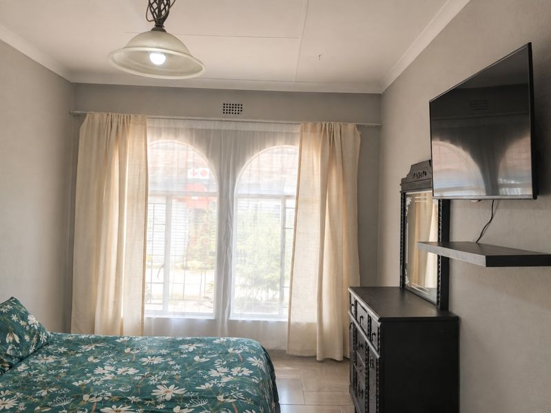 A bedroom featuring arched windows, tiled flooring, and a wall-mounted television, offering a functional space with neutral wall finishes.