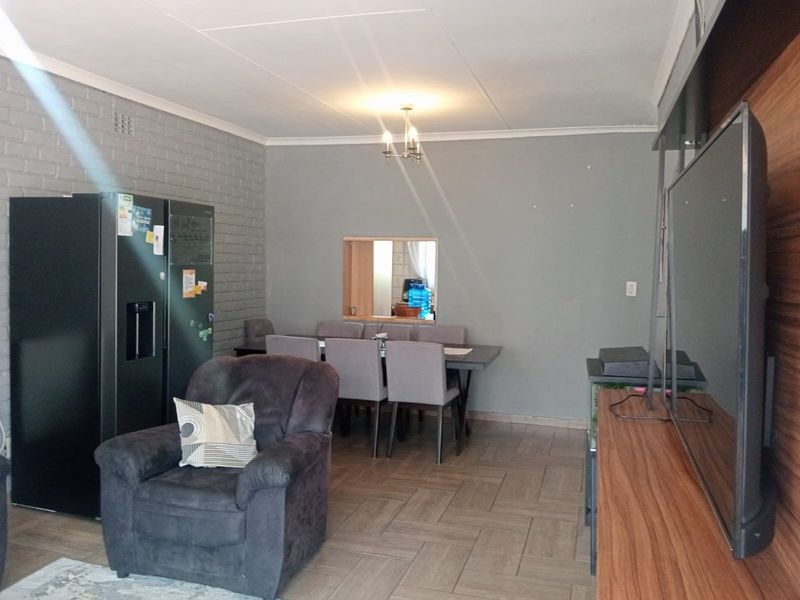Open plan living and dining area featuring a brick accent wall, tiled flooring, and a convenient serving hatch connecting to the kitchen.