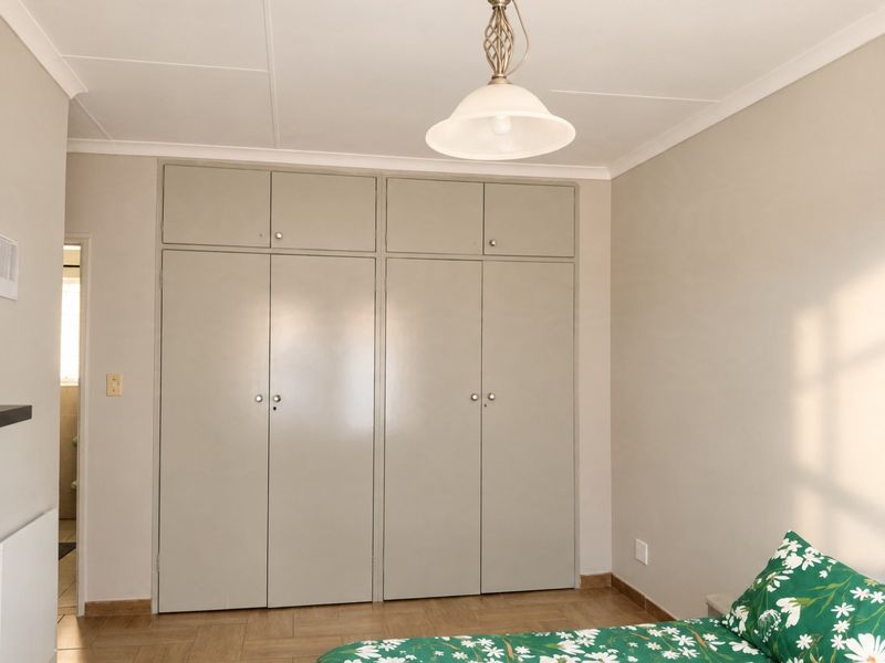 A bedroom featuring neutral walls, tiled flooring, and ample built-in cupboard storage with overhead cabinets.