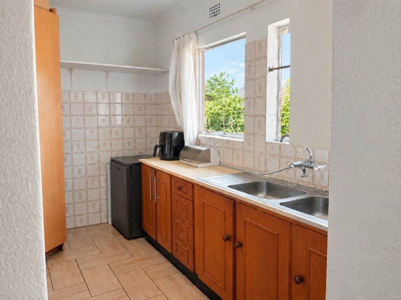 A functional scullery area featuring wooden cabinetry, a double stainless steel sink, tiled splashbacks, and tiled flooring, providing practical utility space.