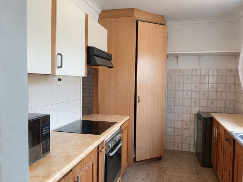 A functional kitchen featuring laminate countertops, built-in oven, electric hob, extractor fan, and ample cabinetry with tiled backsplash and flooring.