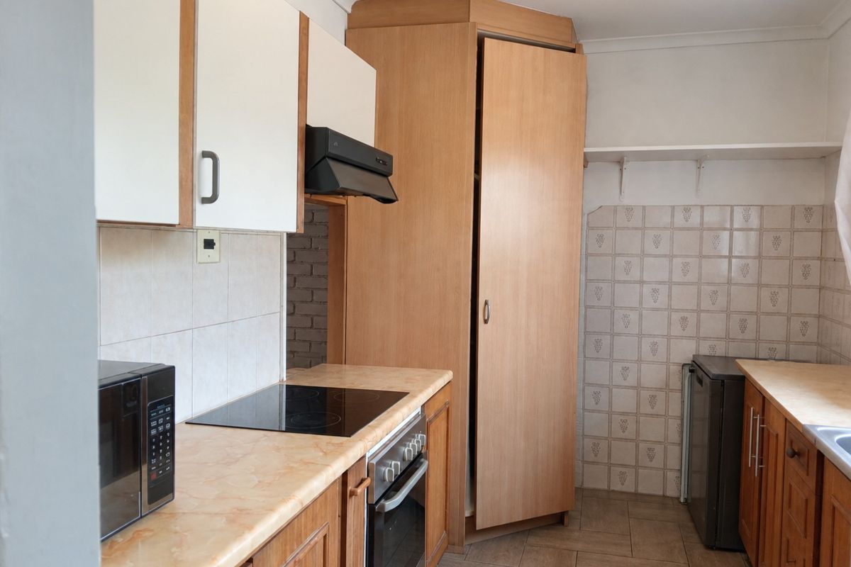 A functional kitchen featuring laminate countertops, built-in oven, electric hob, extractor fan, and ample cabinetry with tiled backsplash and flooring.