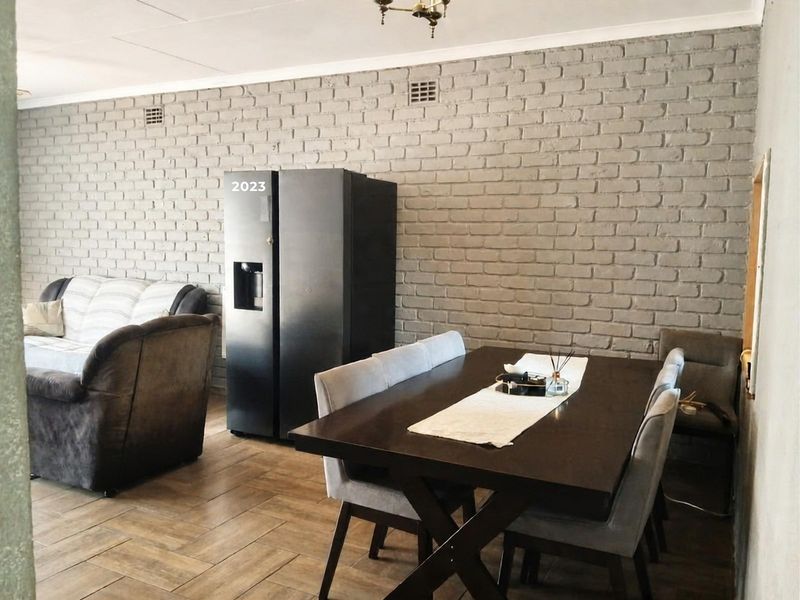 Open plan living and dining area featuring a textured exposed brick feature wall and durable tiled flooring.
