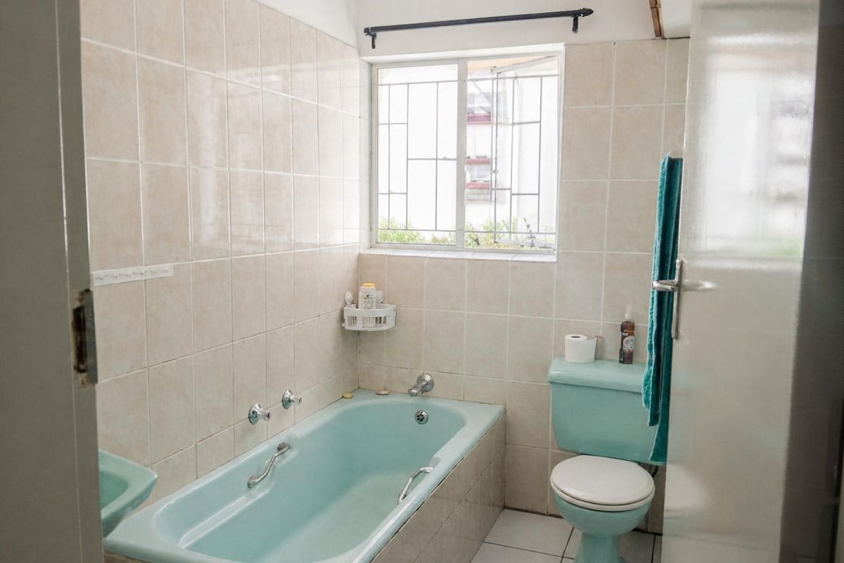 A functional bathroom featuring a vintage-style bathtub and toilet, complemented by neutral wall tiling and a window with security bars.