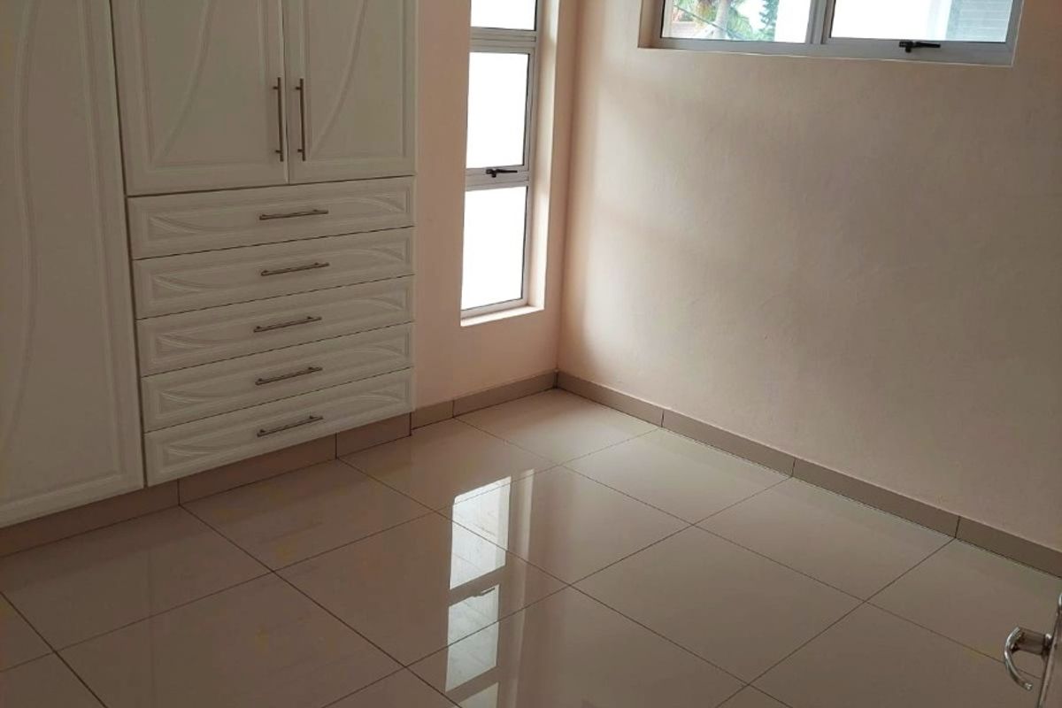 A bright, empty bedroom featuring neutral tiled flooring and ample built-in cupboard storage with modern white cabinetry.