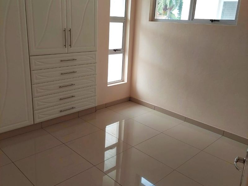 A bright, empty bedroom featuring neutral tiled flooring and ample built-in cupboard storage with modern white cabinetry.