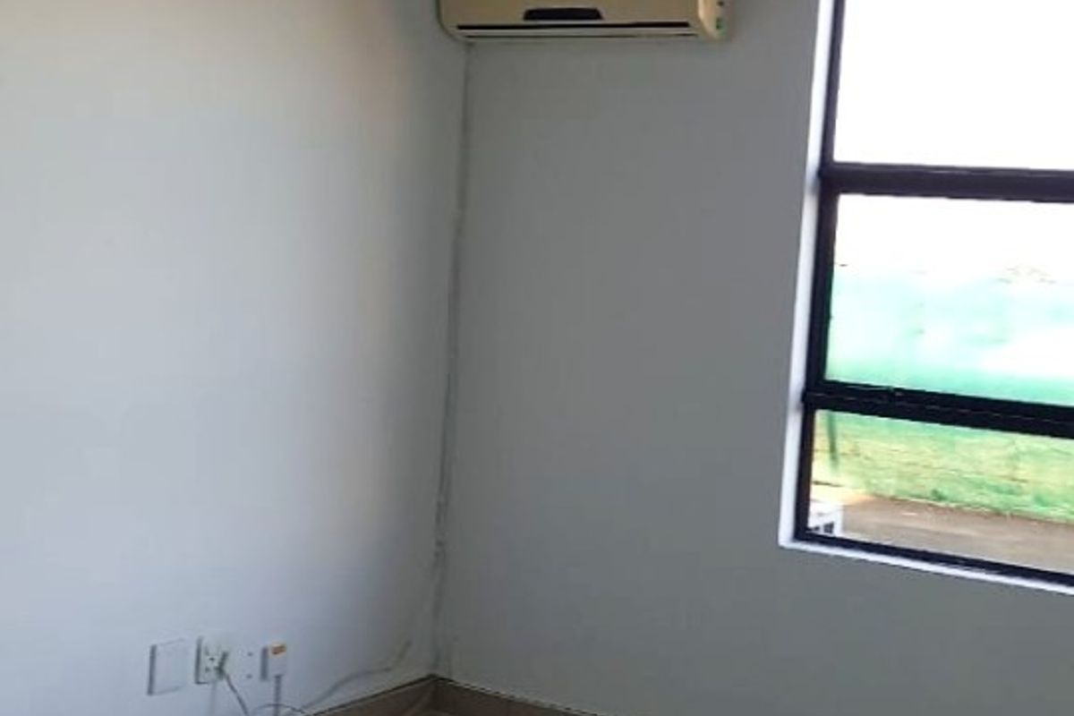 An empty living area featuring tiled flooring, a wall-mounted air conditioning unit, and a large window with natural light.
