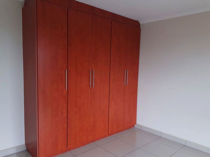 A clean, empty bedroom featuring floor-to-ceiling built-in wooden cupboards and neutral tiled flooring.