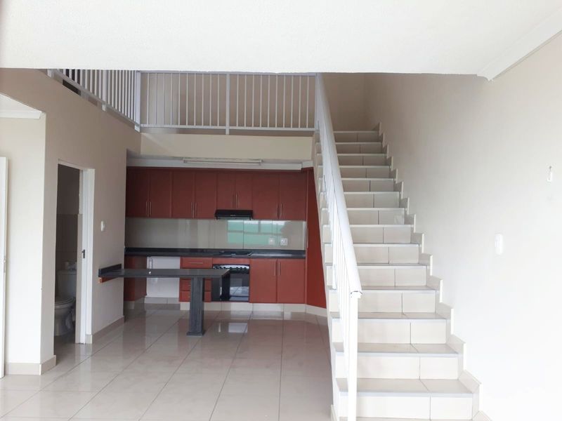 Open-plan living area featuring a tiled kitchen with built-in cabinetry, oven, and hob, adjacent to a staircase leading to an upper level.