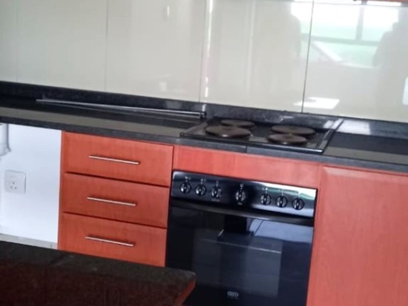 A functional kitchen featuring wood-finish cabinetry, granite countertops, a built-in oven, electric hob, and a modern glass splashback with tiled flooring.