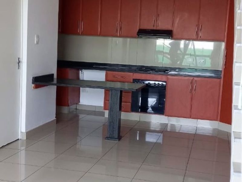 Open-plan kitchen featuring built-in cabinetry, integrated oven and hob, breakfast bar, and tiled flooring, with a mezzanine level overlooking the space.