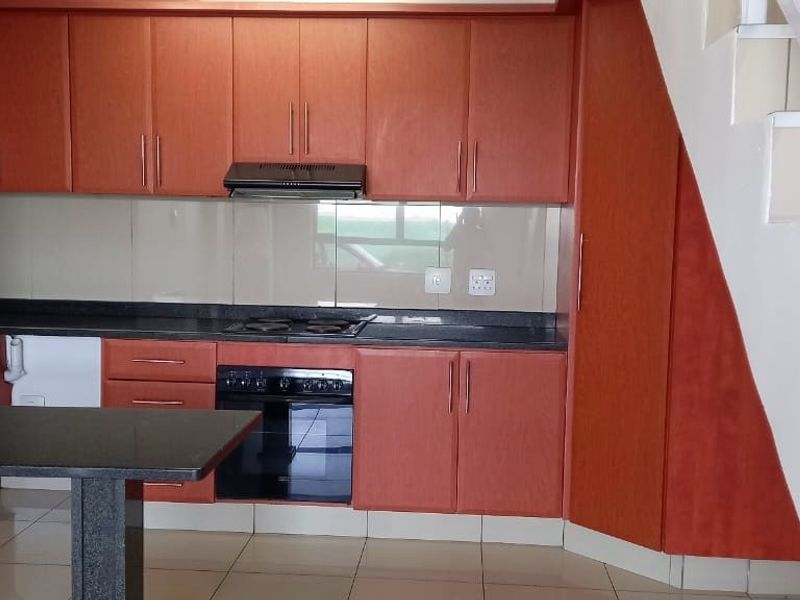 A functional kitchen featuring wood-finish cabinetry, granite countertops, integrated oven and hob, and tiled flooring, conveniently located adjacent to the staircase.