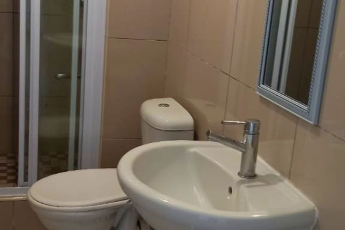 A functional bathroom featuring a pedestal basin, toilet, and a glass-enclosed shower with neutral wall and floor tiling.
