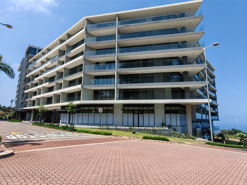 Modern multi-story apartment building featuring extensive glass balustrades, private balconies, and a paved approach.