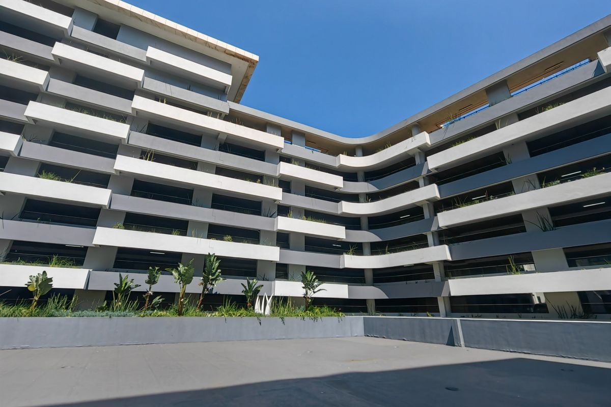 A modern multi-story apartment building exterior featuring tiered balconies with integrated planter boxes and a clean concrete courtyard area.